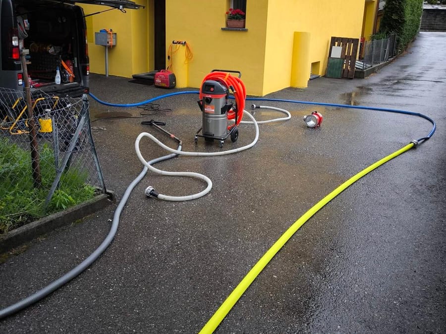 Furgone aperto davanti a una casa, aspiratore e tubi stesi sul piazzale bagnato