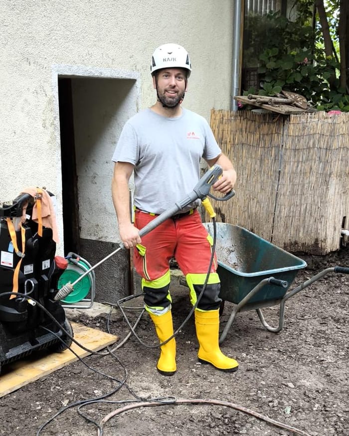 Sergio Marazza in cantiere, con casco e stivali, davanti a un cortile pieno di fango dopo un'alluvione